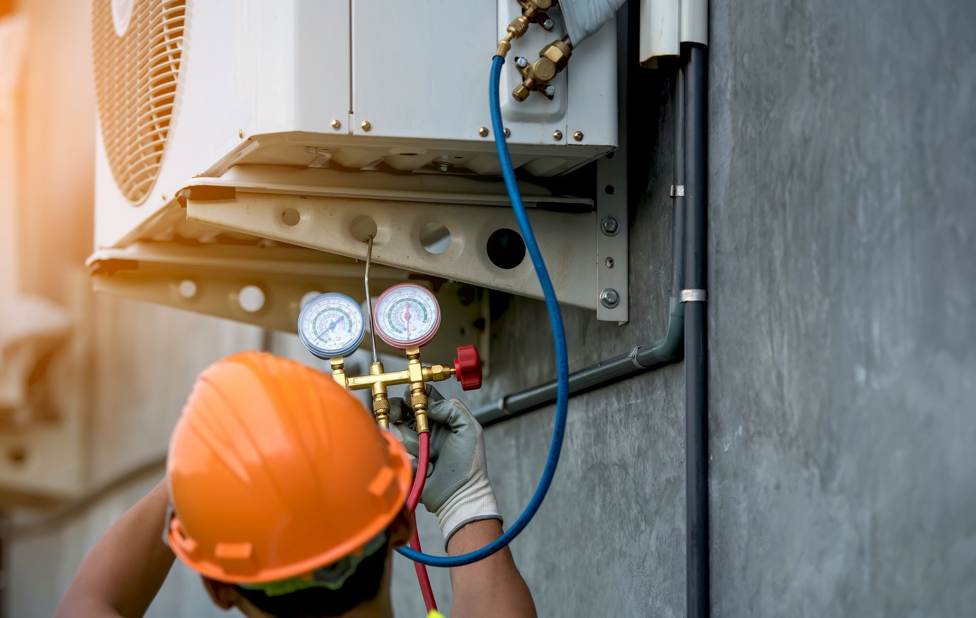 HVAC technician in hard hat repairing air conditioning unit outdoors, using gauges.
