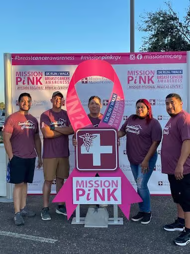 Five people in maroon shirts stand near a large pink ribbon sign for 