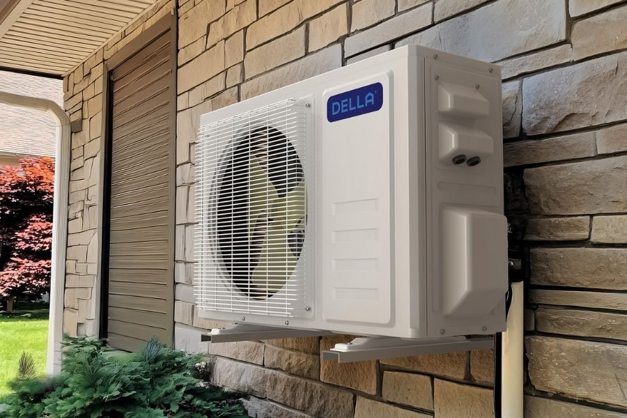 A white Della brand outdoor mini-split air conditioner unit mounted on a stone-faced exterior wall.
