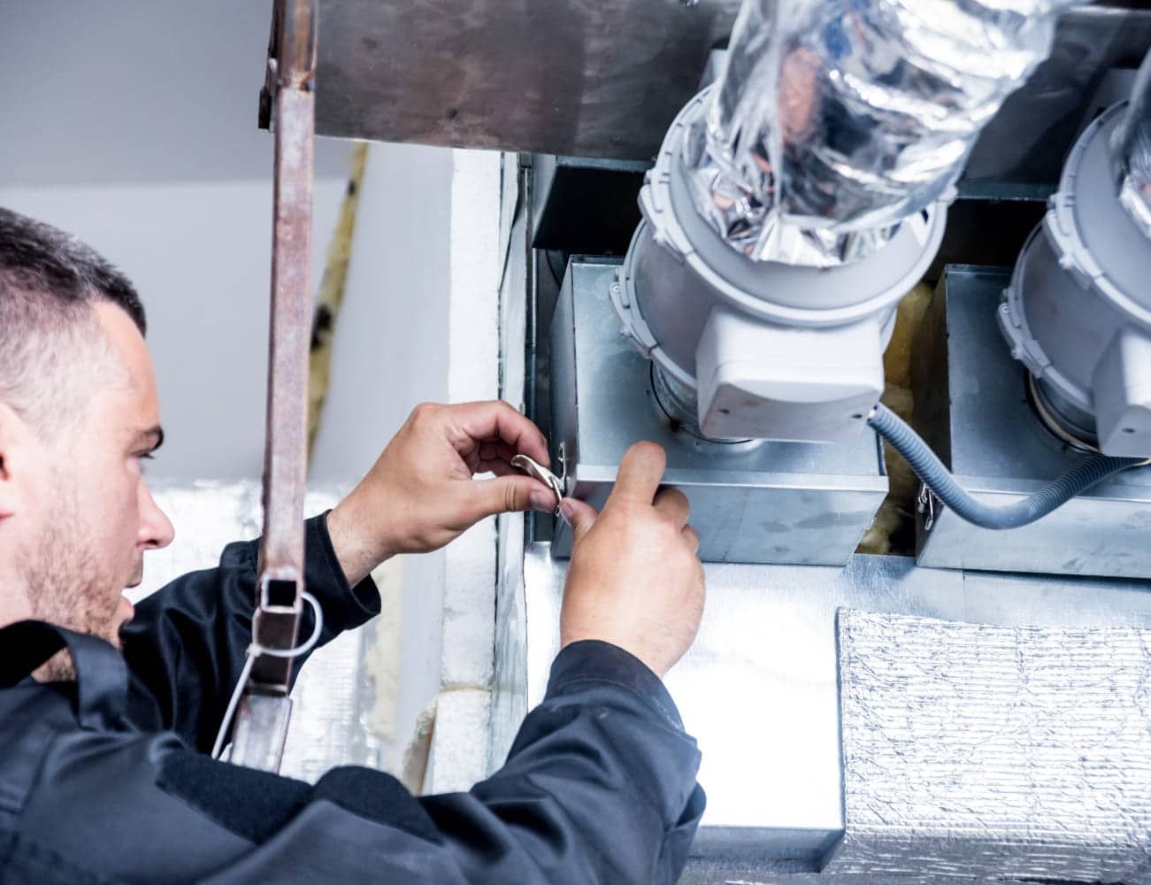 HVAC technician working on ductwork, using tools to connect components in an indoor setting.