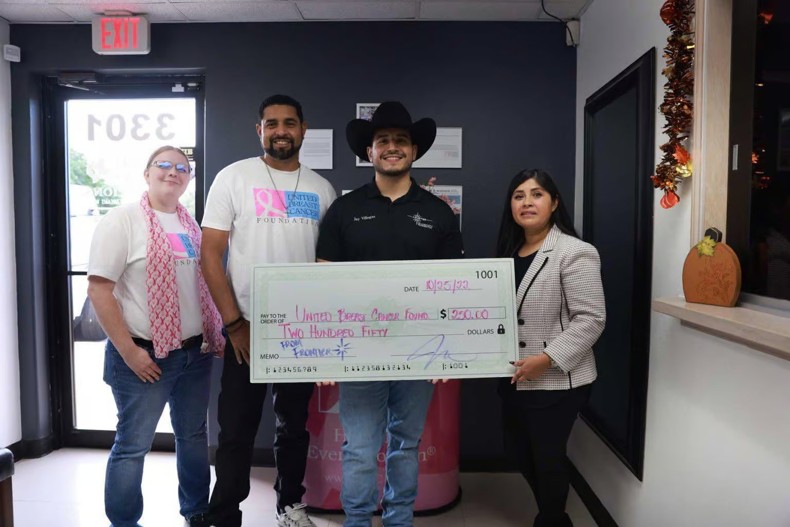 Four people holding a large check indoors, likely a donation.