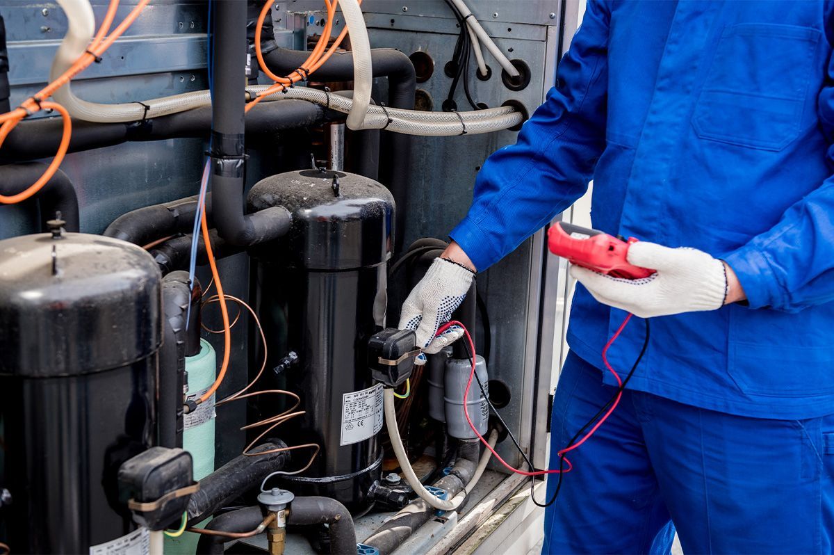HVAC technician in blue overalls tests an air conditioning unit with a multimeter.