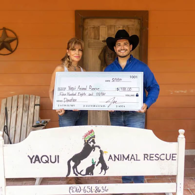 Two people holding a check for Yaqui Animal Rescue in front of a building.