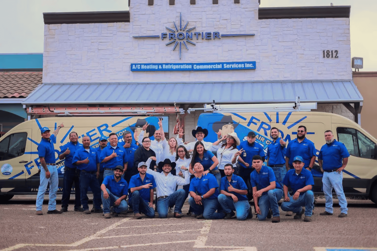 Group of employees in blue shirts posing with Frontier company van and building.