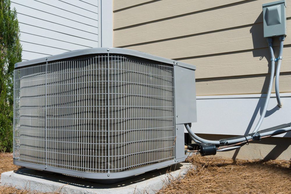 An air conditioning unit sits outside a house with beige siding.