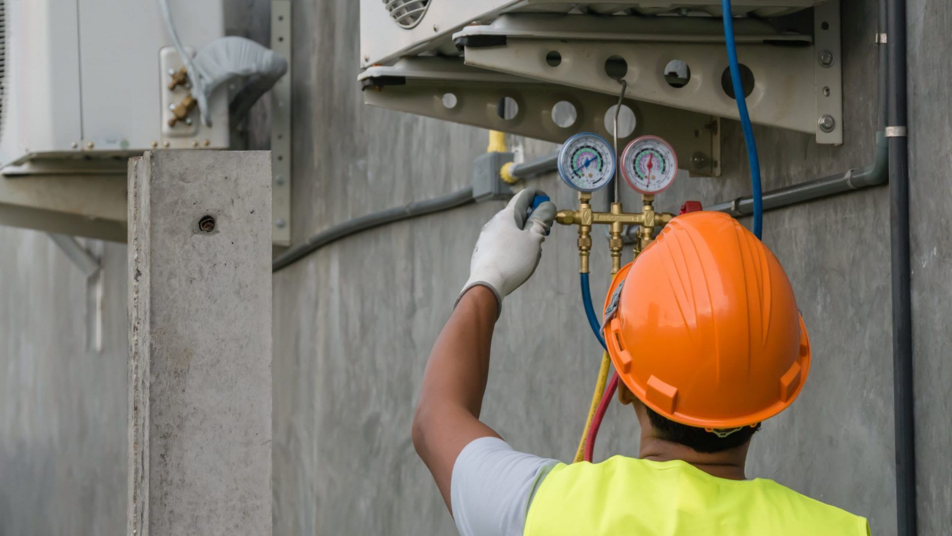 HVAC technician adjusting gauges on an air conditioning unit. Wearing a hard hat and gloves.