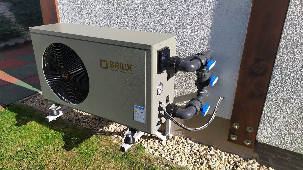 Outdoor heat pump unit mounted beside a building, with pipes and cables connected.