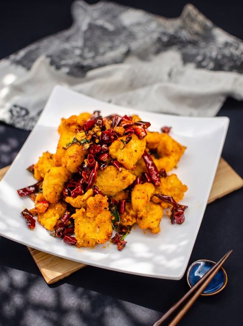 Crispy golden fried chicken bites topped with red chilies on a white square plate