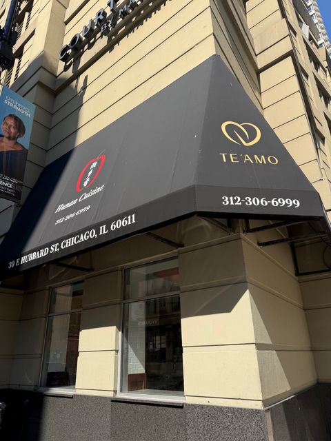 Storefront with a black awning and gold logo on a city building corner, with a phone number displayed