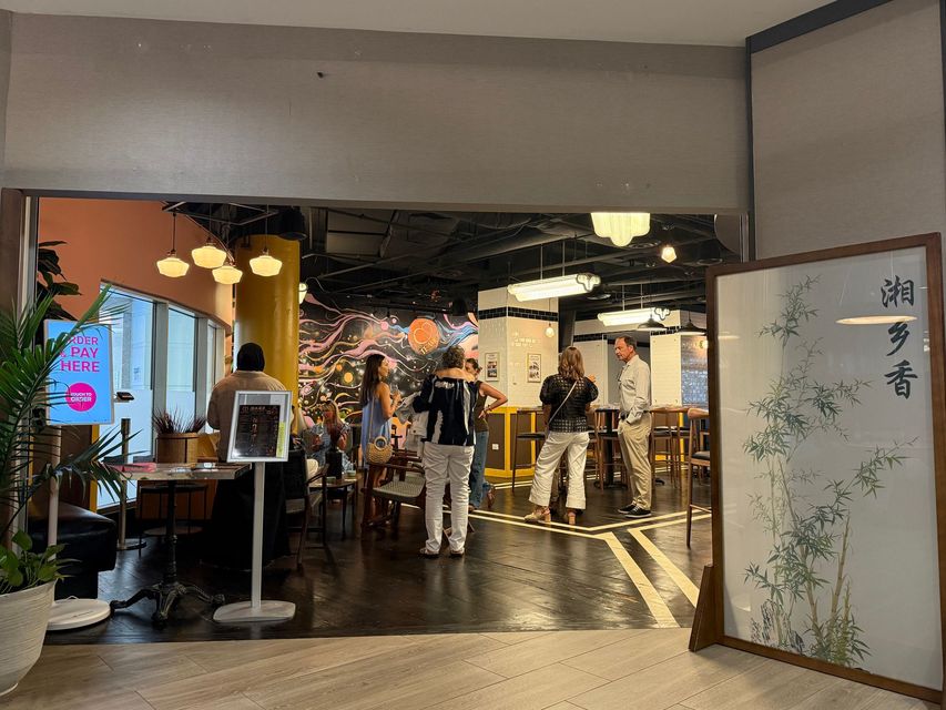 Busy restaurant entrance with diners, warm lights, and a decorative screen with Japanese calligraphy