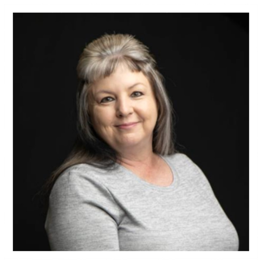 Portrait of a smiling woman with gray hair in a gray top against a black background