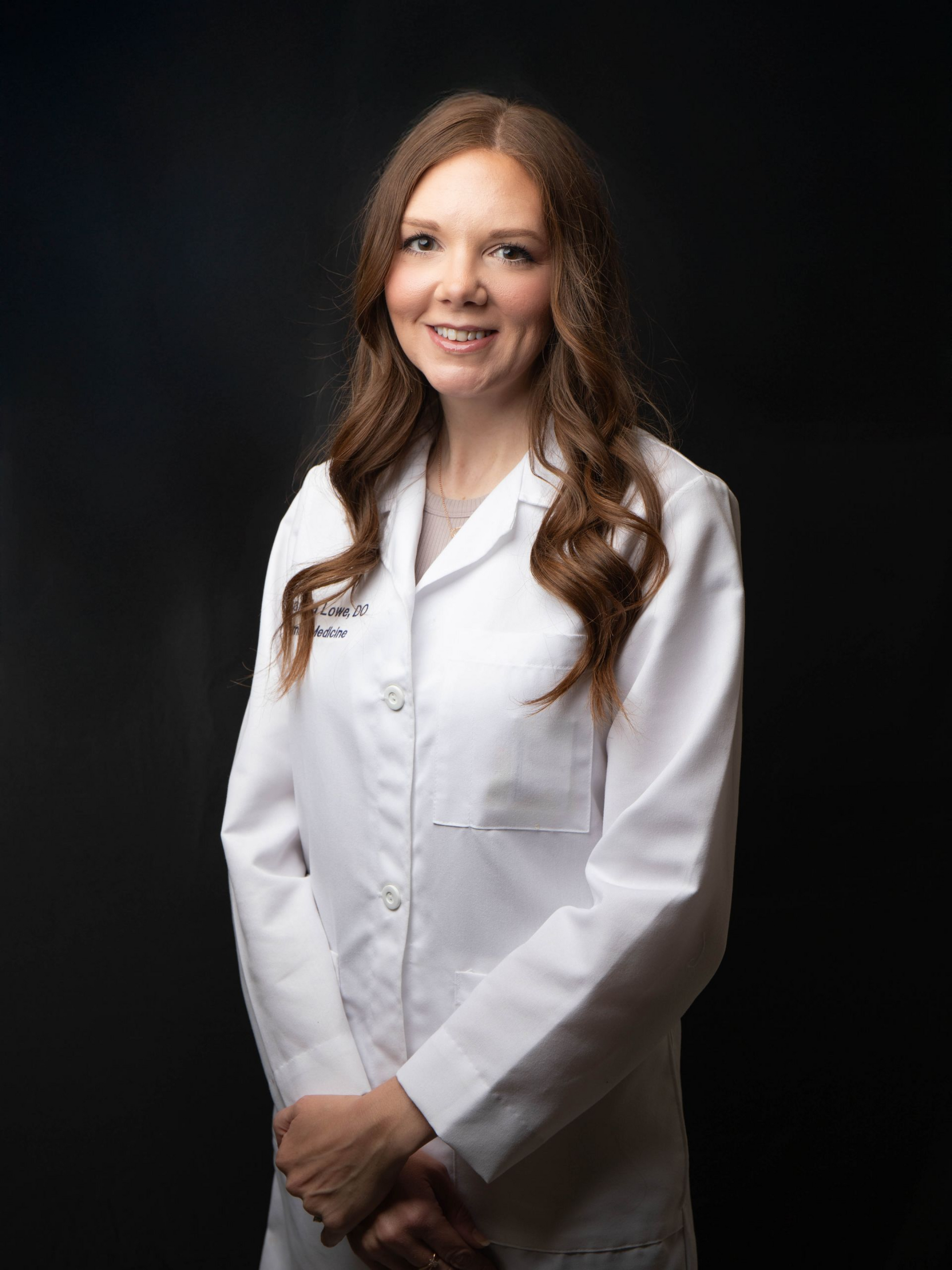 Woman in a white coat smiling against a black background