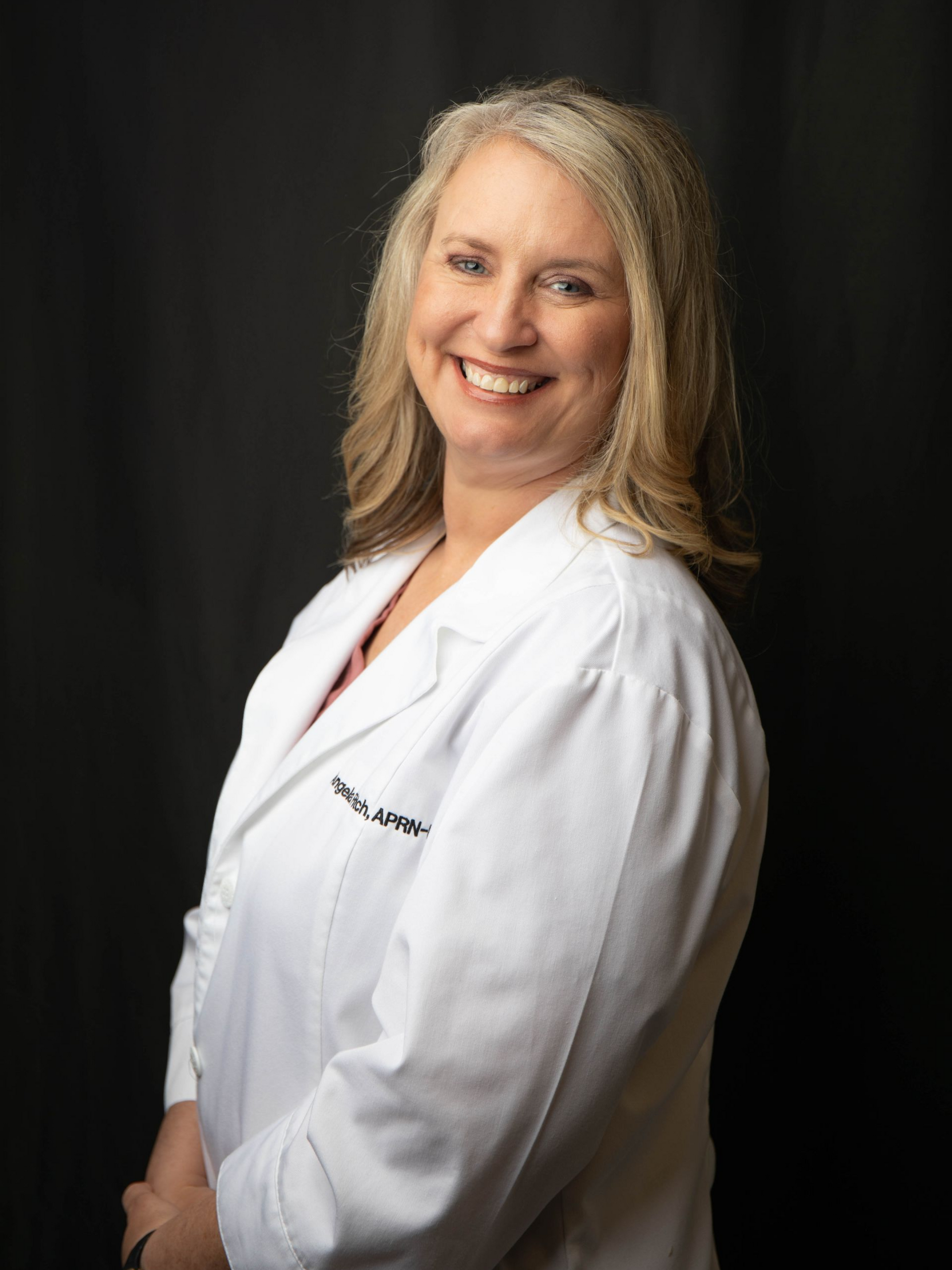 Smiling woman in a white lab coat over a navy top against a black background