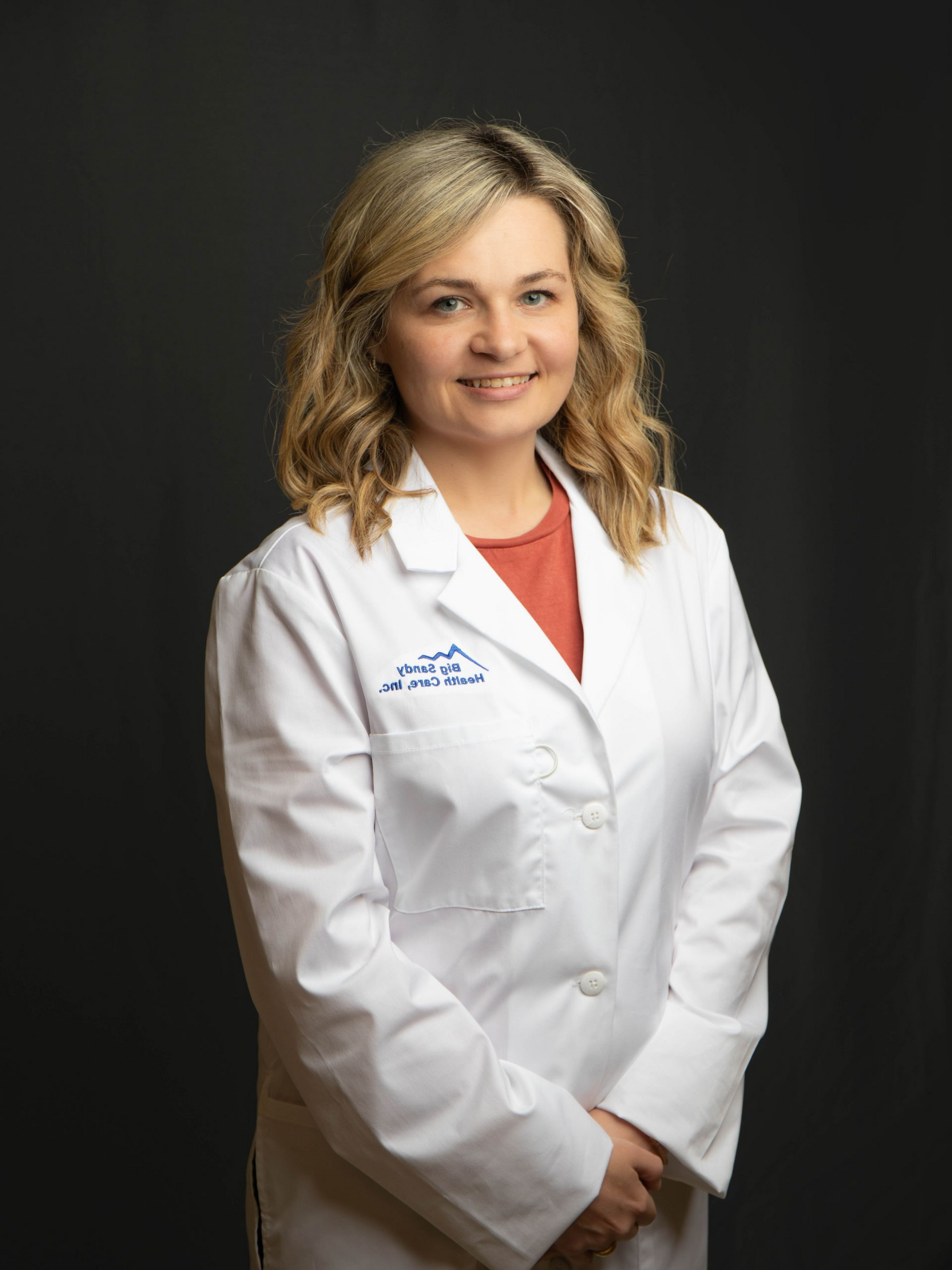 Professional portrait of a person in a white coat over a blue top, smiling against a black background