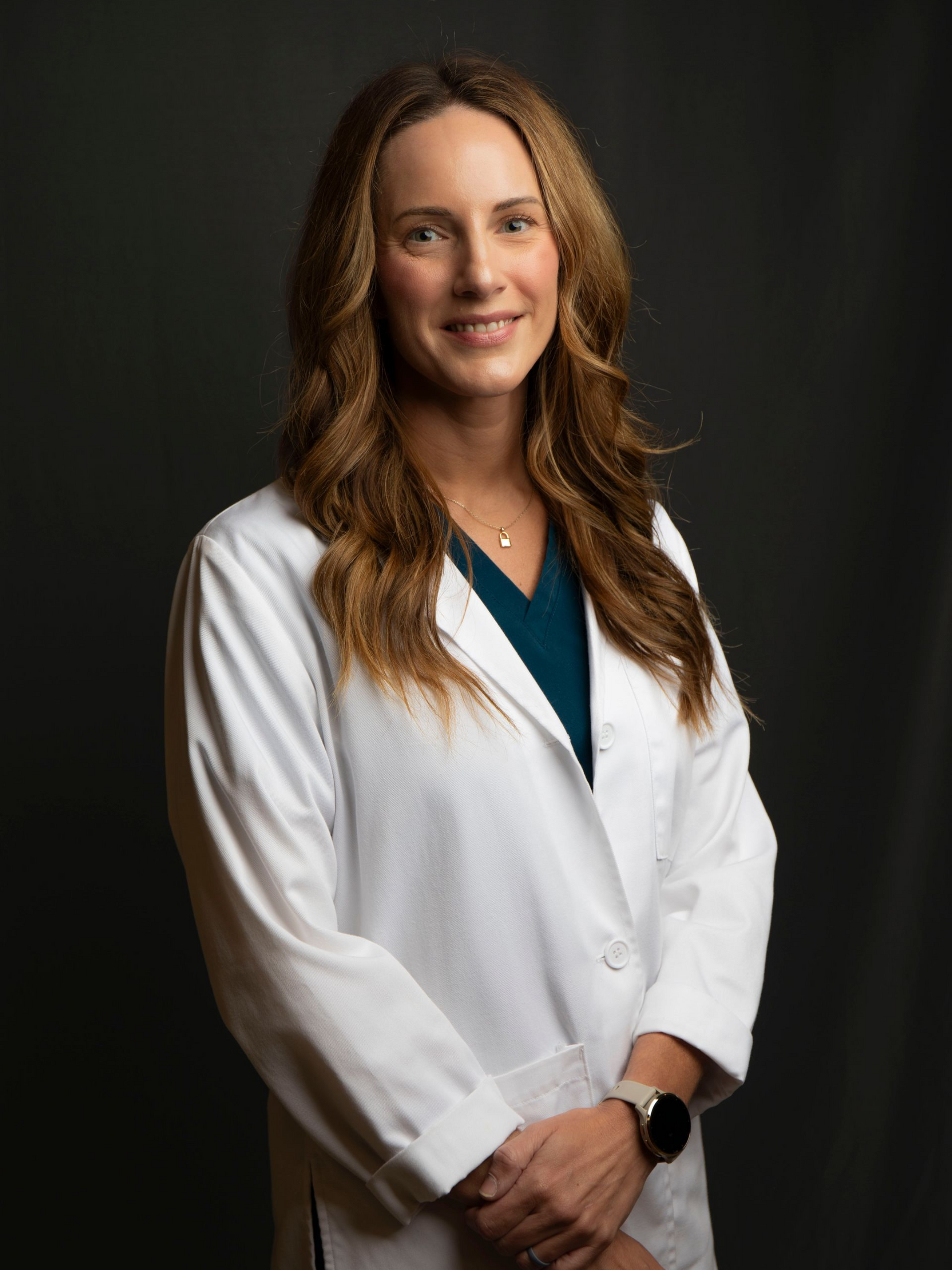 Woman in a white lab coat standing against a black background and smiling softly