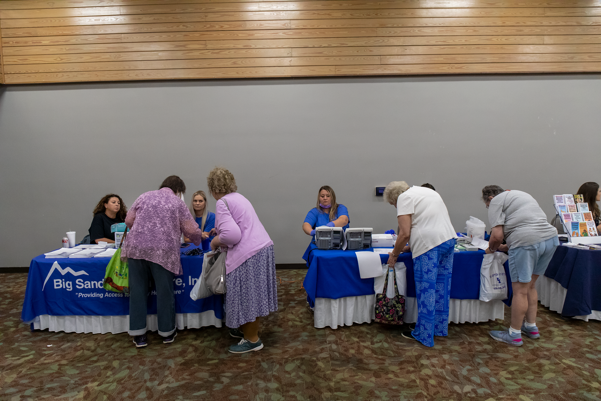 People at a community event table, signing up and handing out materials in a hall