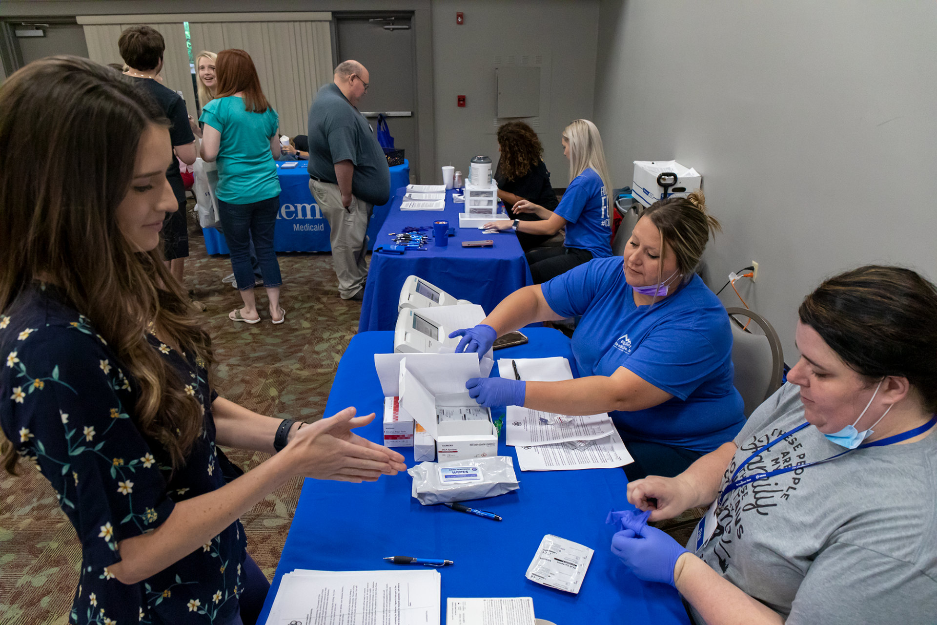 People at a blue-covered registration table with laptops and papers in a community room