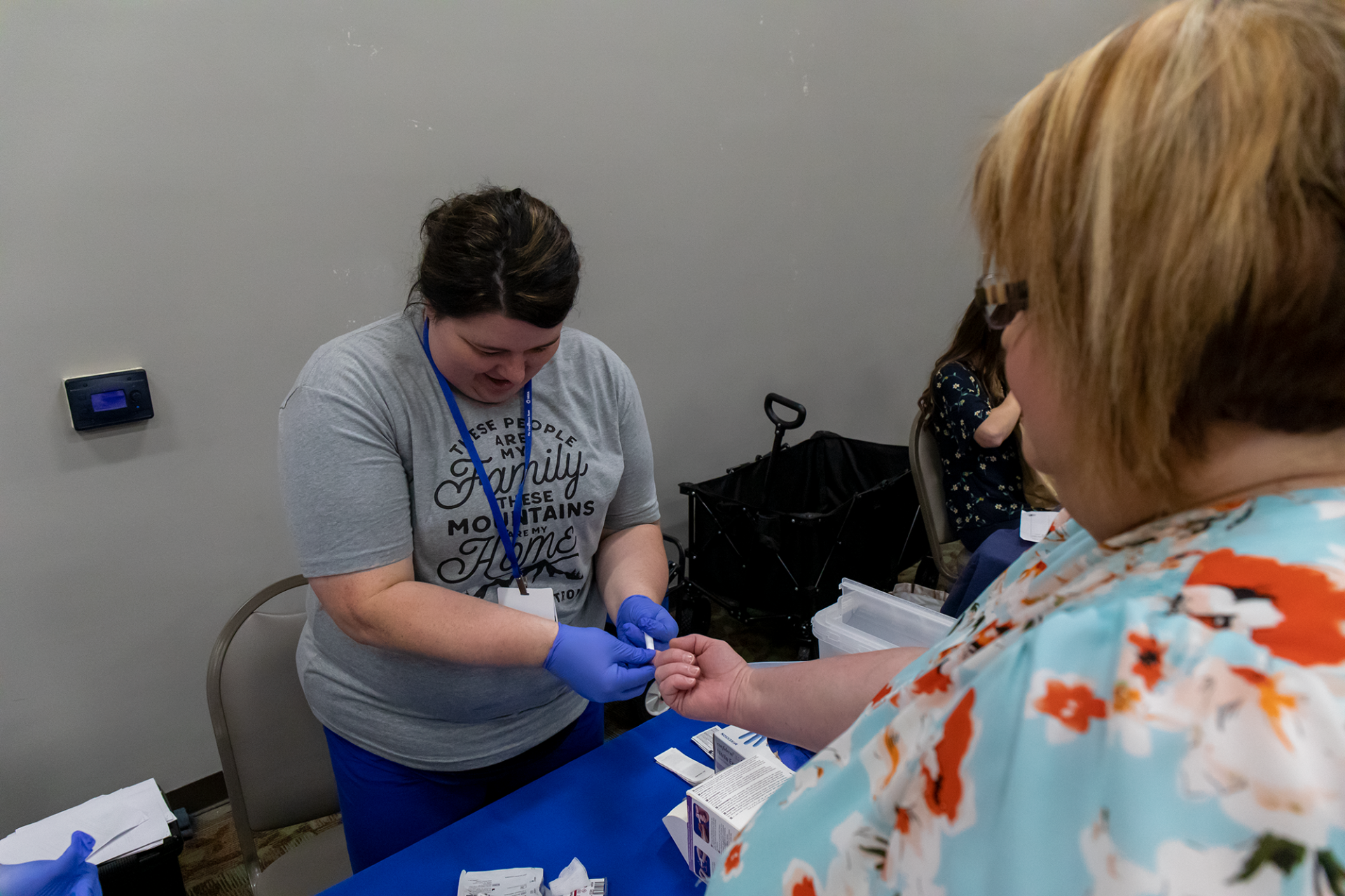 Volunteer at a table putting on blue gloves while handing something to a visitor in a room