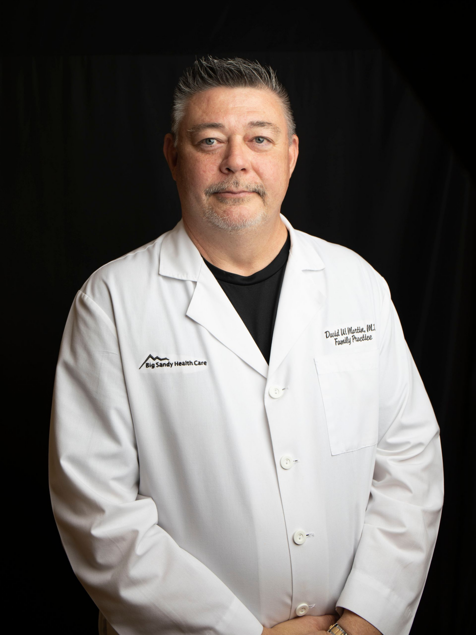 Doctor in white coat with stethoscope smiling against a dark background