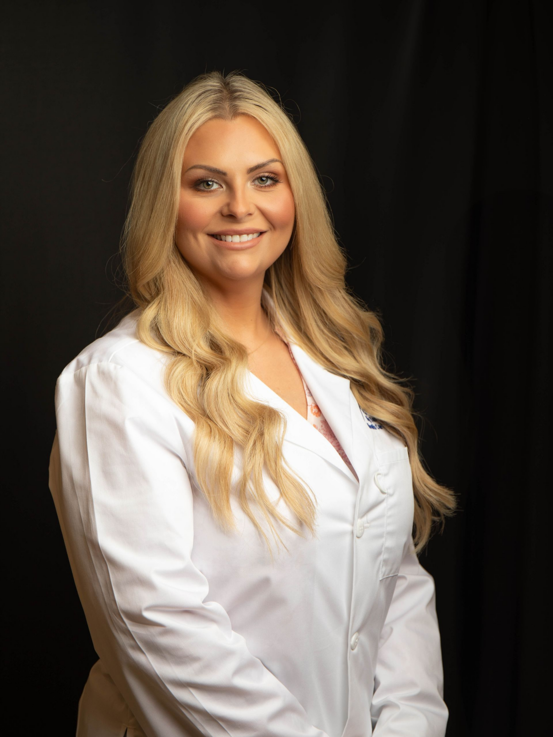 Smiling blonde woman in a white blazer against a dark background