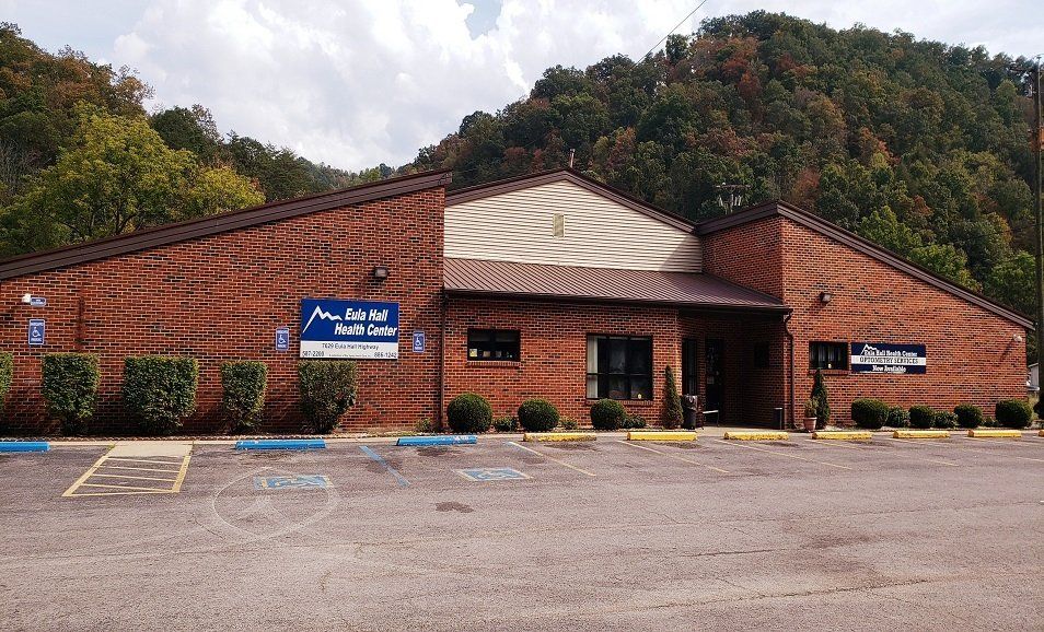 Brick building with blue signs in a wooded mountain setting, viewed across an empty parking lot