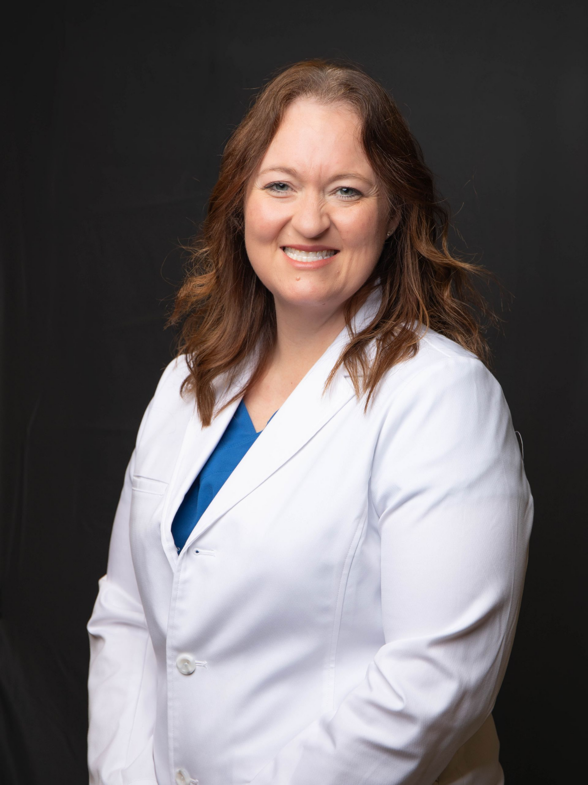 Woman in a white lab coat smiling against a dark background.