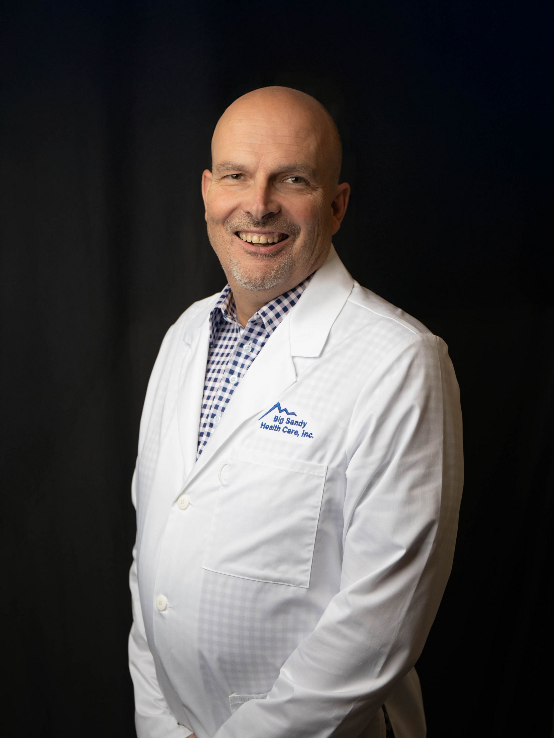 Smiling bald man in a blue Kentucky pullover against a dark background