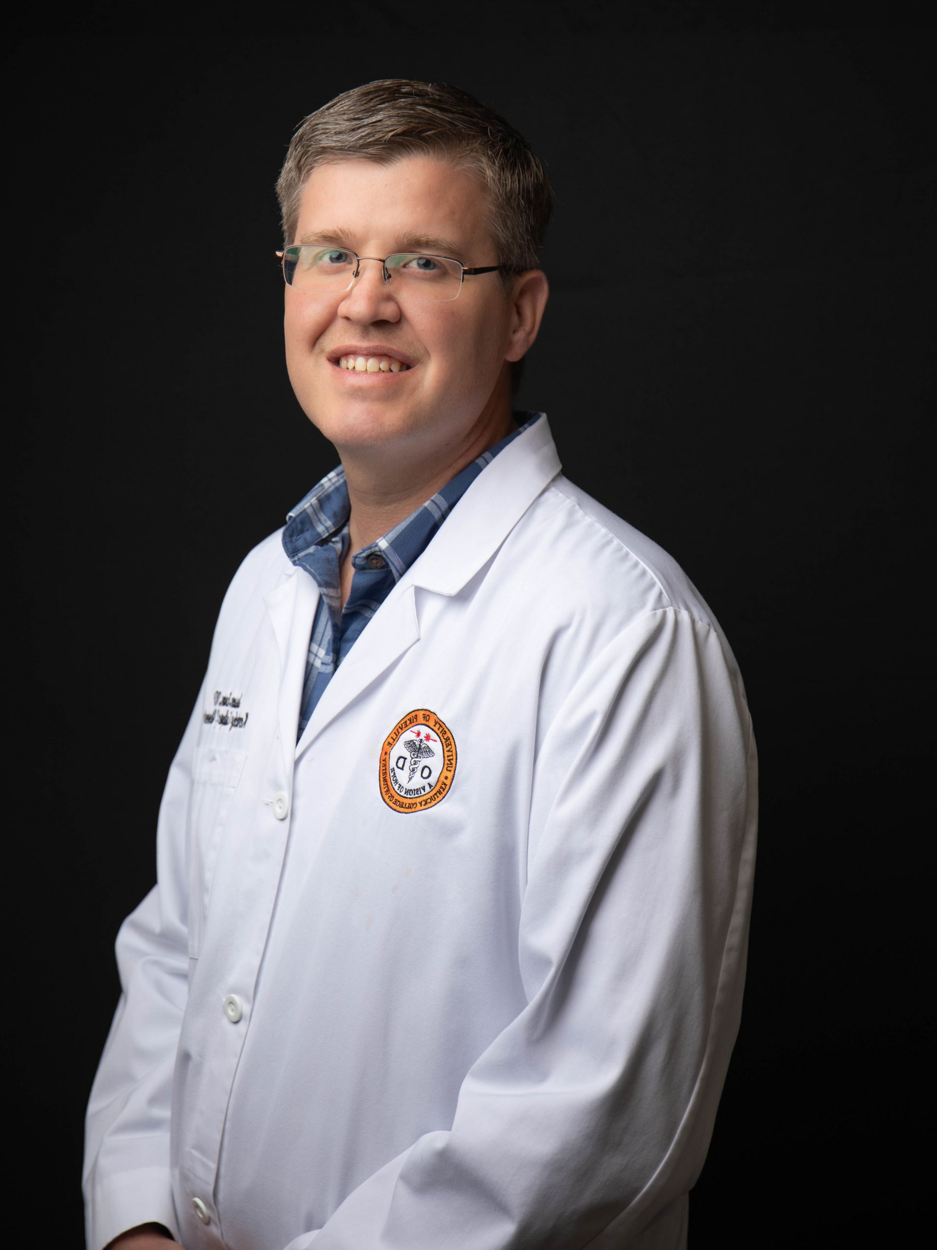 Smiling doctor in white coat and glasses against a dark background