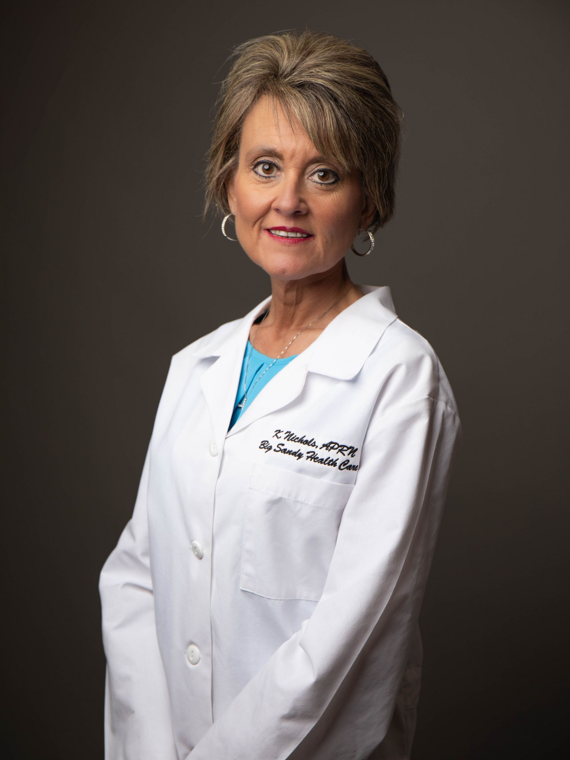Woman in white lab coat and magenta top against black background, wearing a pink necklace.