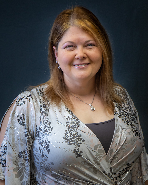 Smiling woman in a silver patterned blouse against a dark studio background