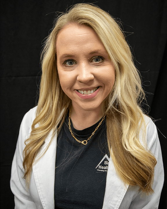 Portrait of a smiling woman in a white coat and black shirt against a dark background