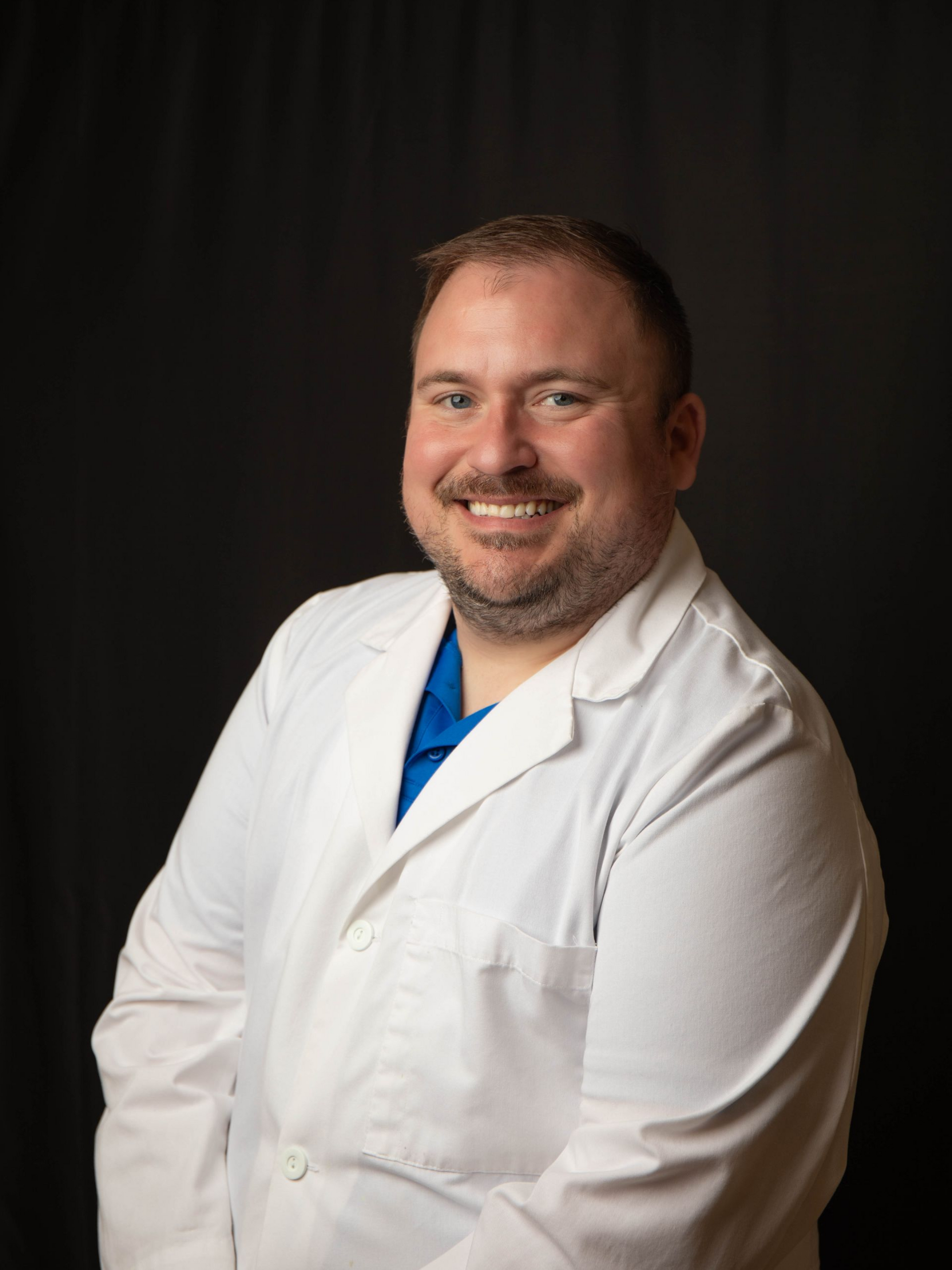 Smiling person in blue scrubs against a dark background