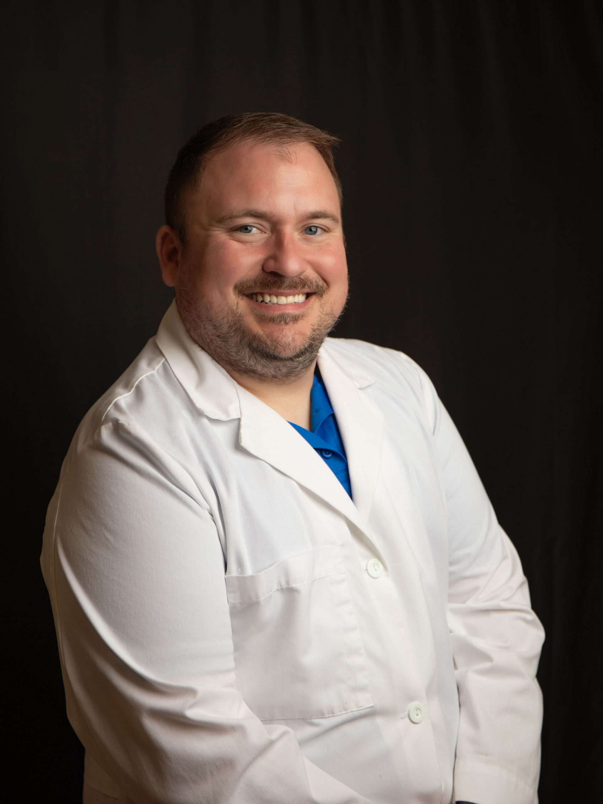 Smiling person in blue scrubs against a dark background