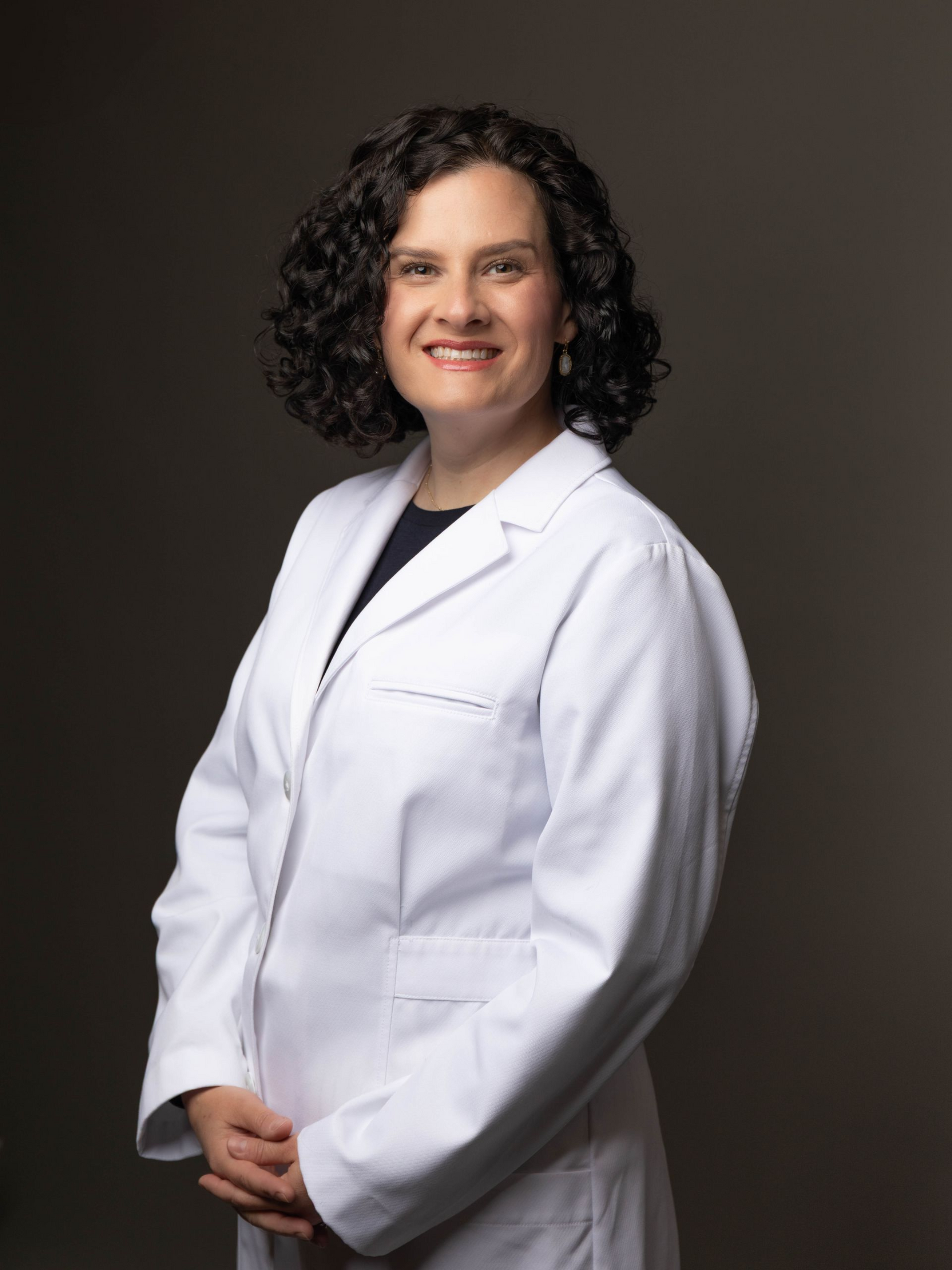 Professional headshot of a smiling doctor in a white coat with a stethoscope against a dark background