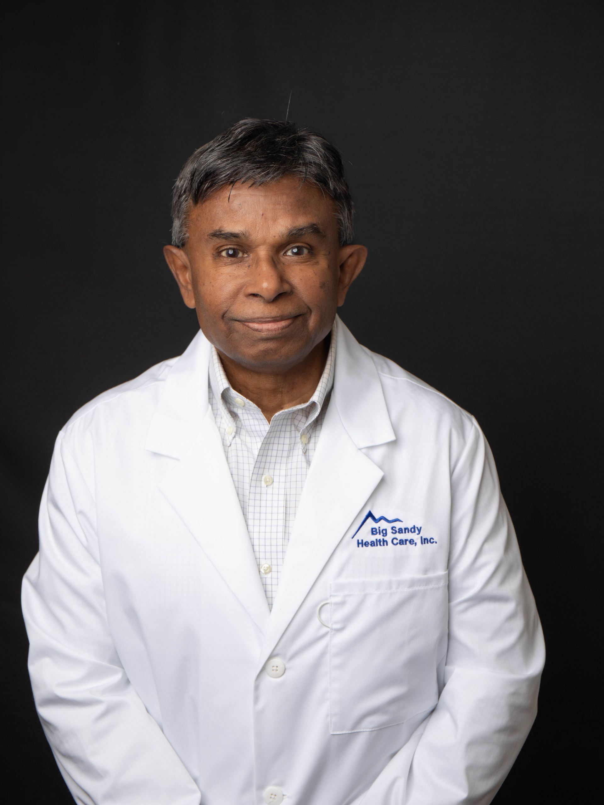 Smiling doctor in a white coat and blue shirt against a dark background