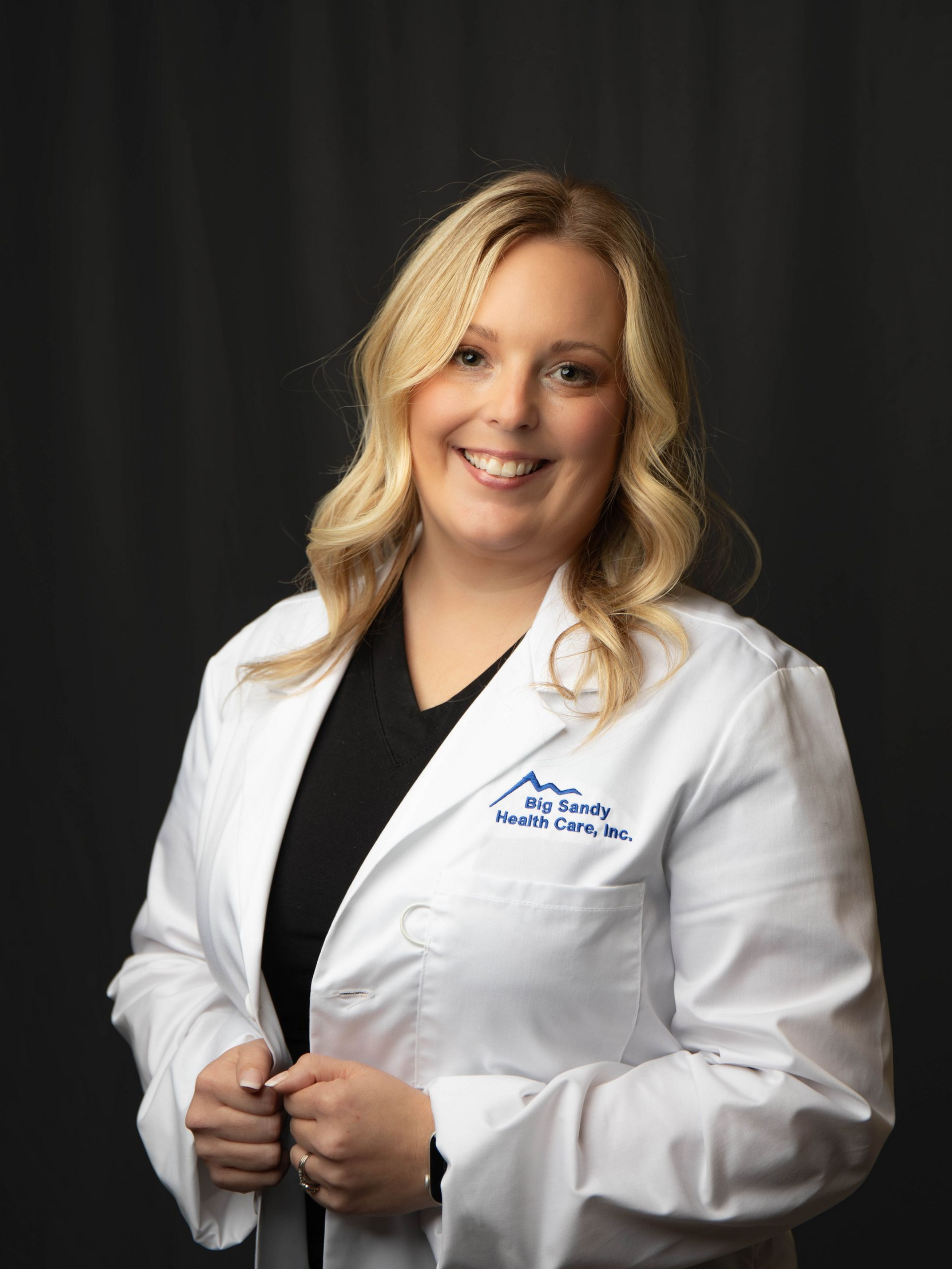 Smiling doctor in white coat with stethoscope against a dark background