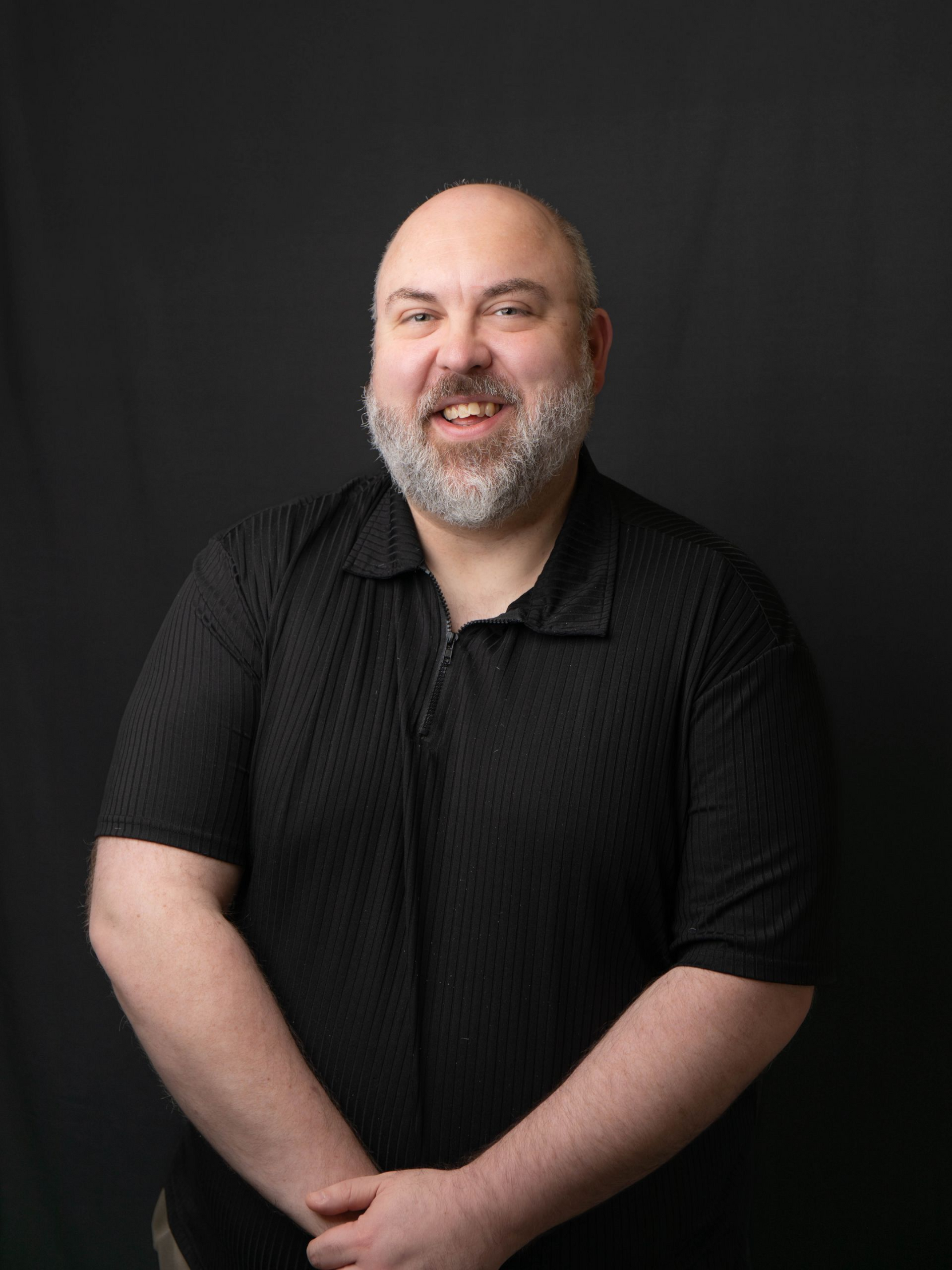 Smiling bald man with glasses in a colorful plaid shirt against a black background
