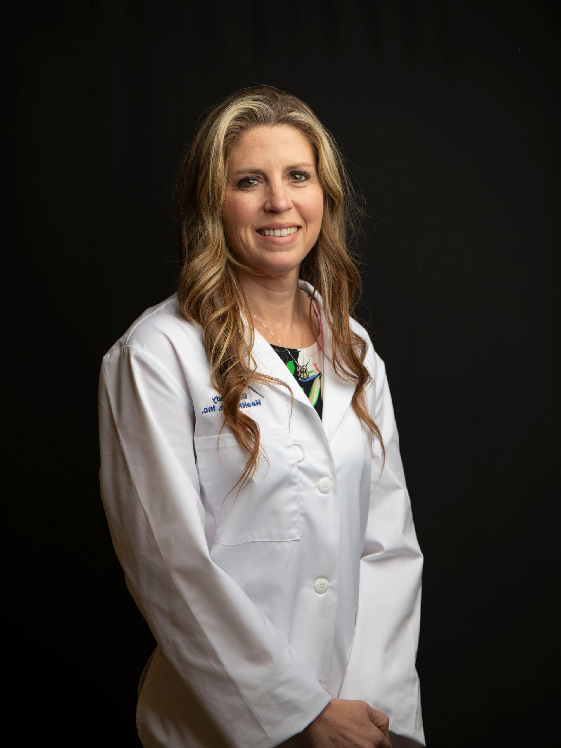 Woman in a white coat smiling against a black background.