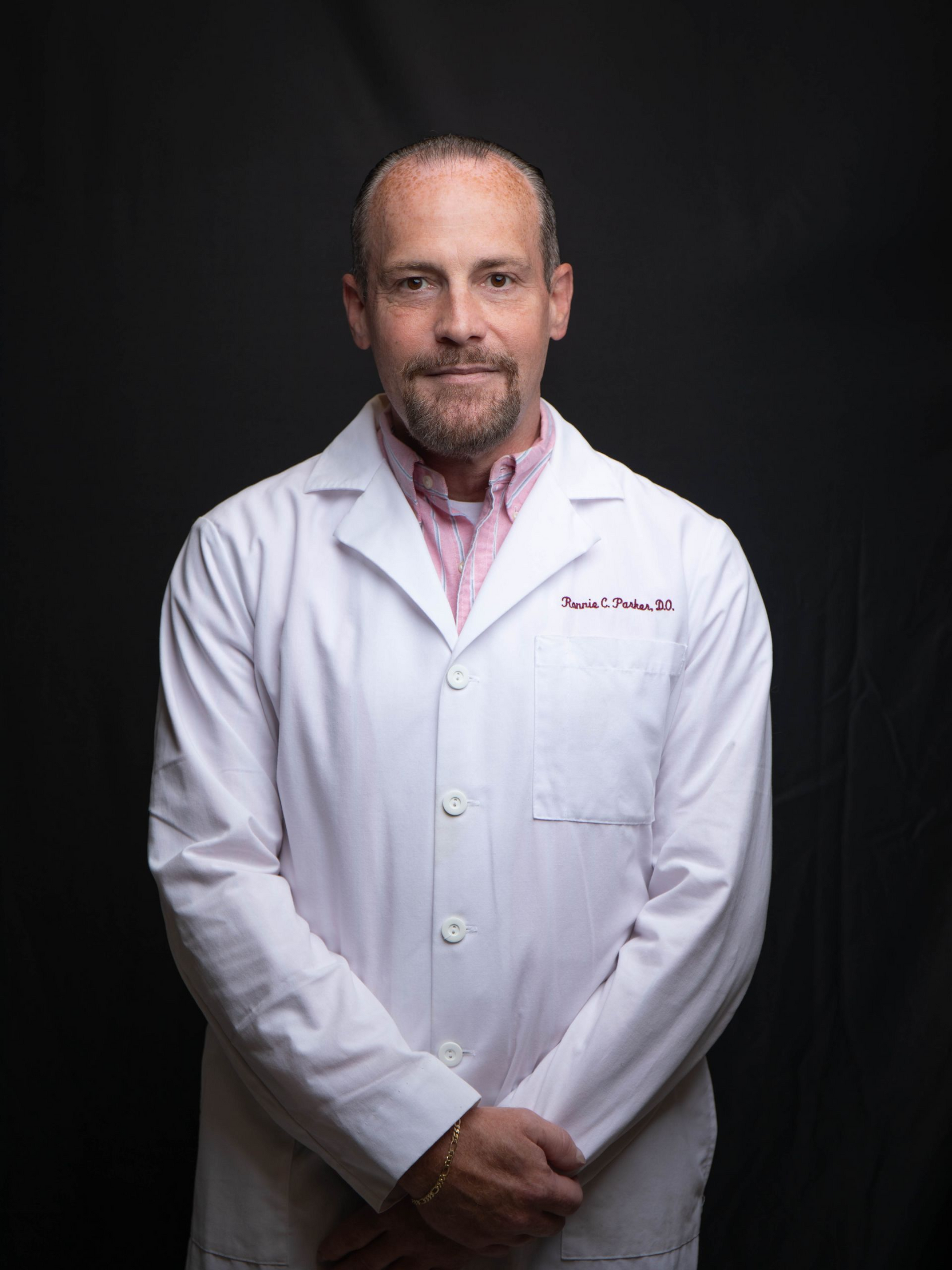 Smiling doctor in a white coat with a pink stethoscope against a black background