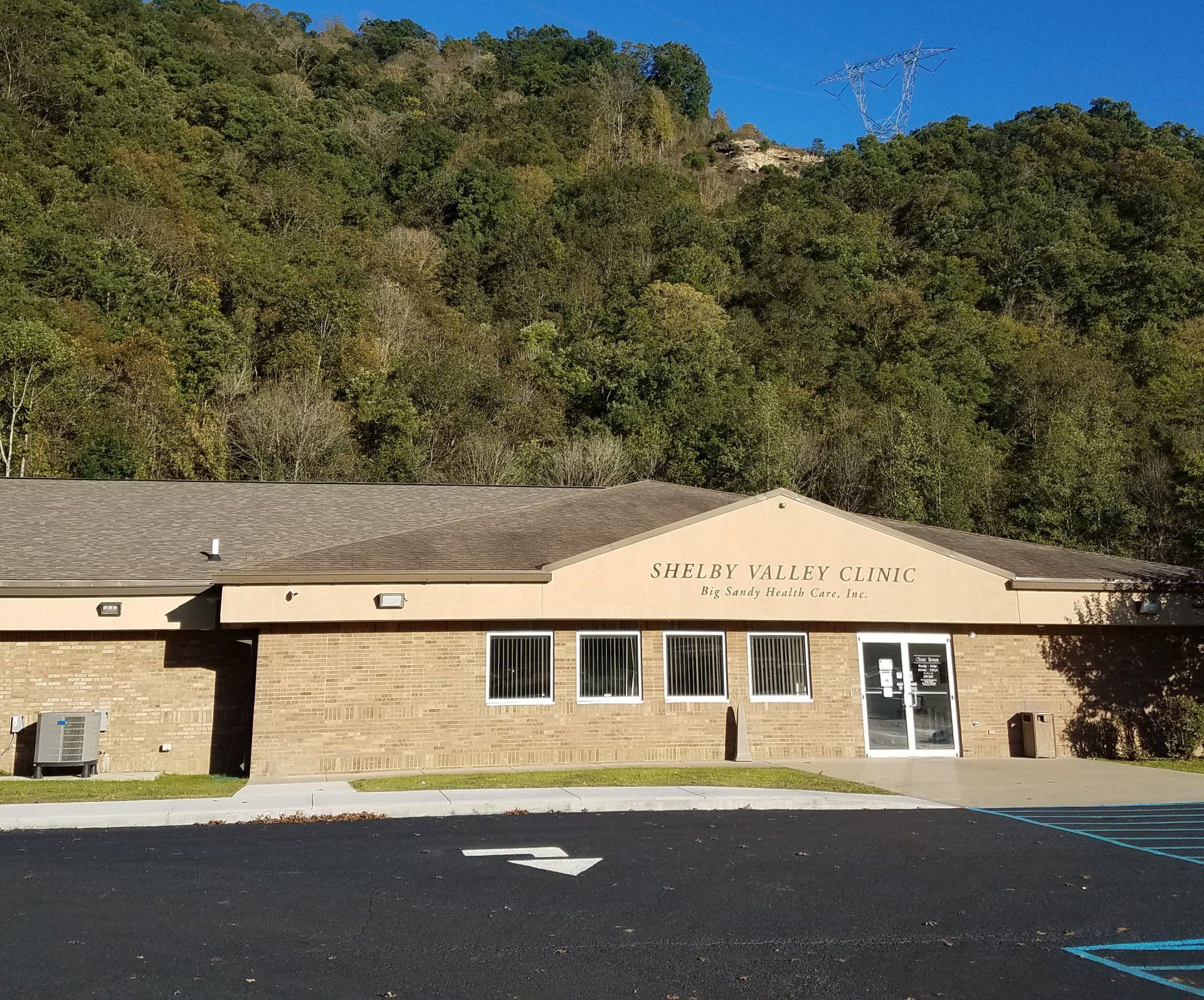 Low tan building with sign in front of wooded hillside and parking lot