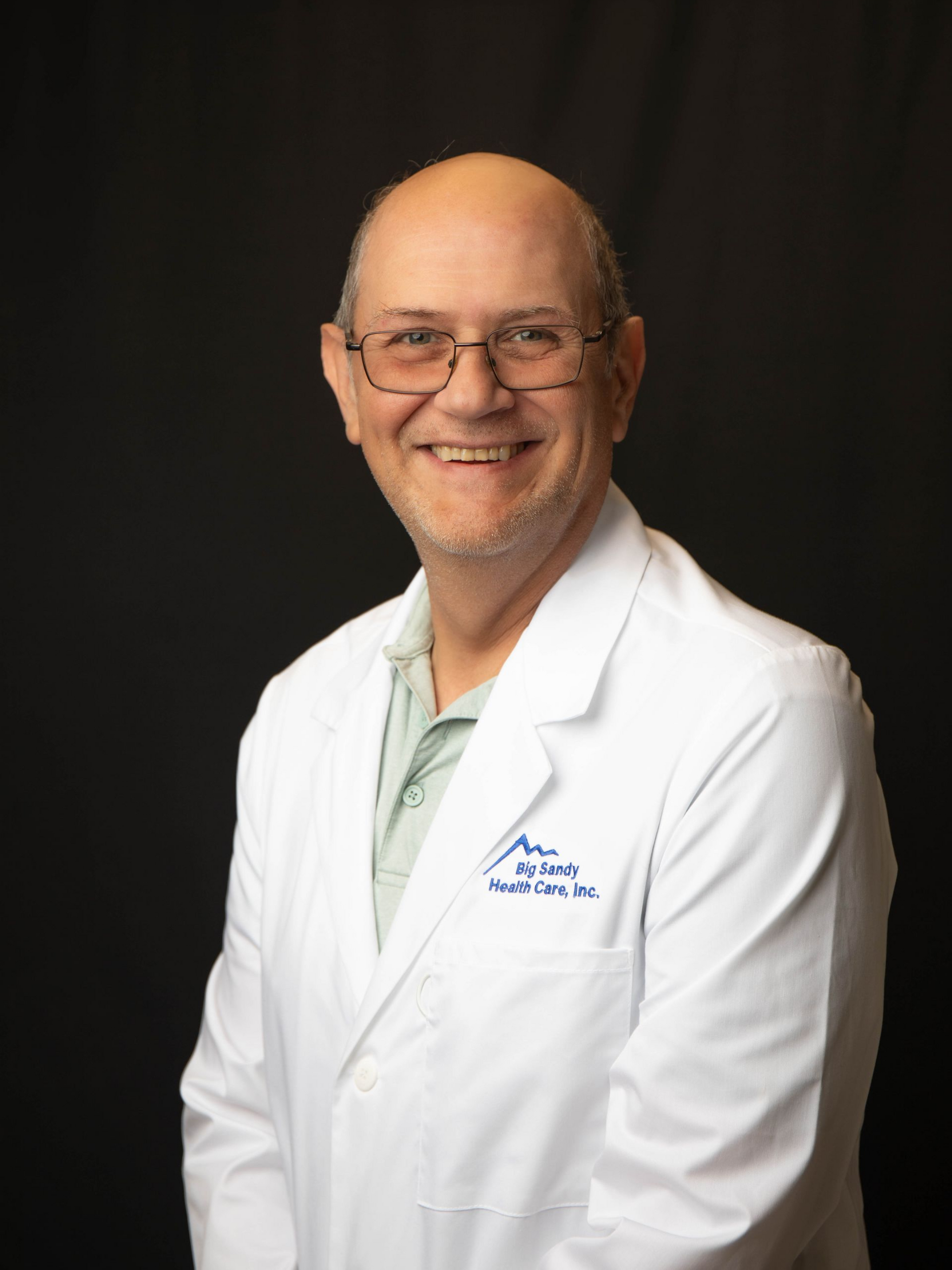 Smiling man in a white lab coat and blue shirt against a black background