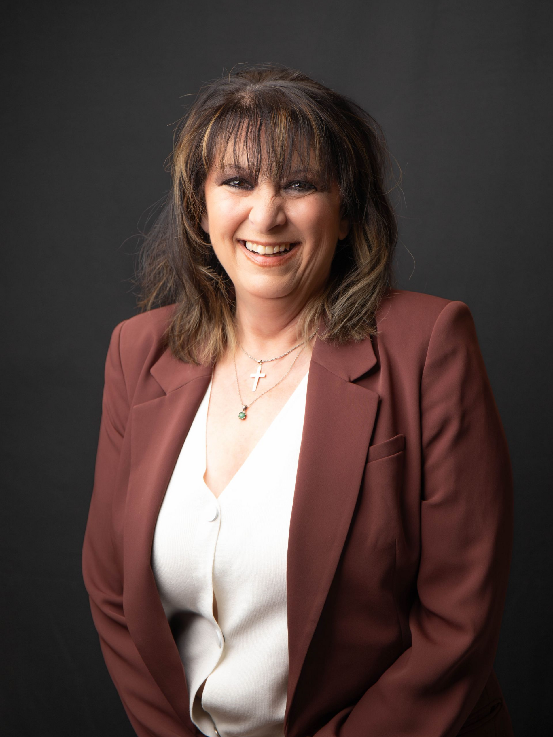 Smiling woman in a black blazer and patterned blouse against a dark background