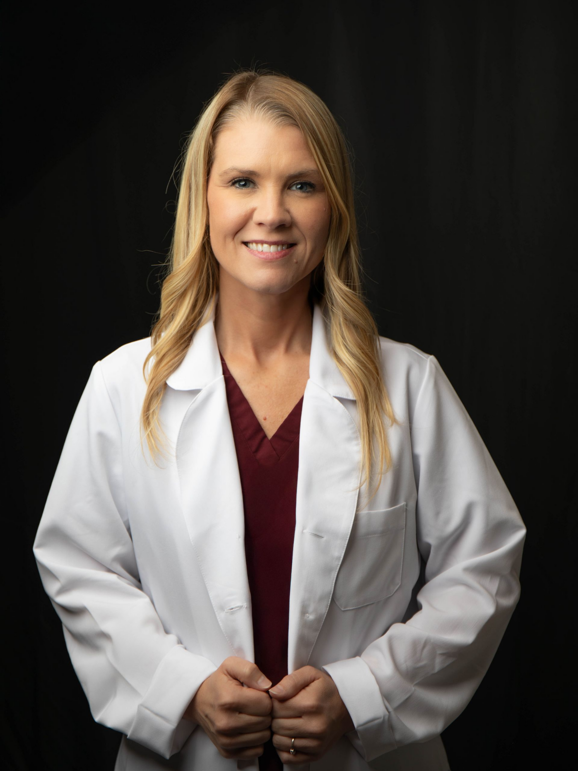 Smiling professional in white coat and red turtleneck against a black background