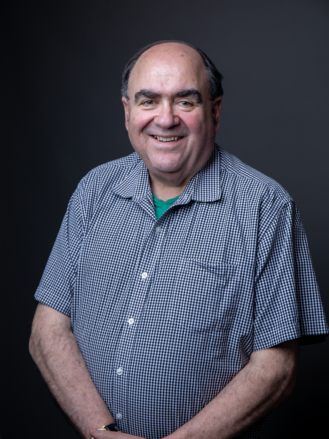 Smiling man in glasses and a dark jacket against a black backdrop