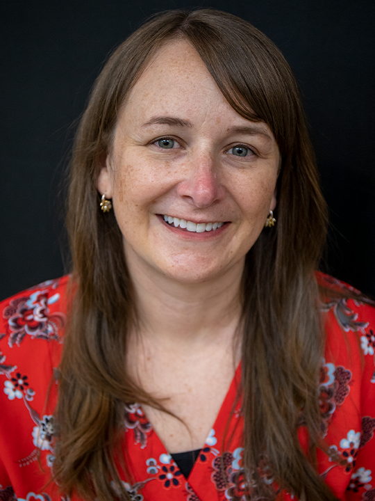 Smiling woman in a red floral blouse against a dark background