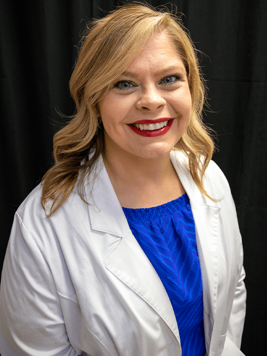 Smiling woman in white coat over blue blouse against a black background