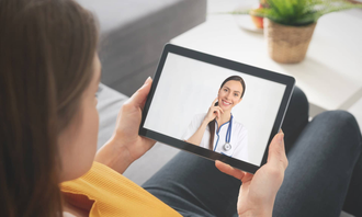 Person video chatting with a doctor on a tablet while sitting on a couch