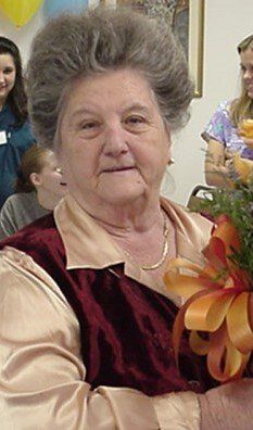 Older woman in a burgundy dress holding a bouquet of orange flowers at an indoor celebration