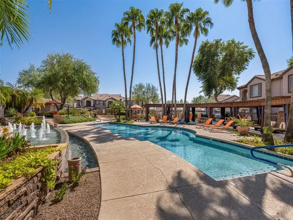 Luxury swimming pool and fountains with lounge chairs and palm trees.