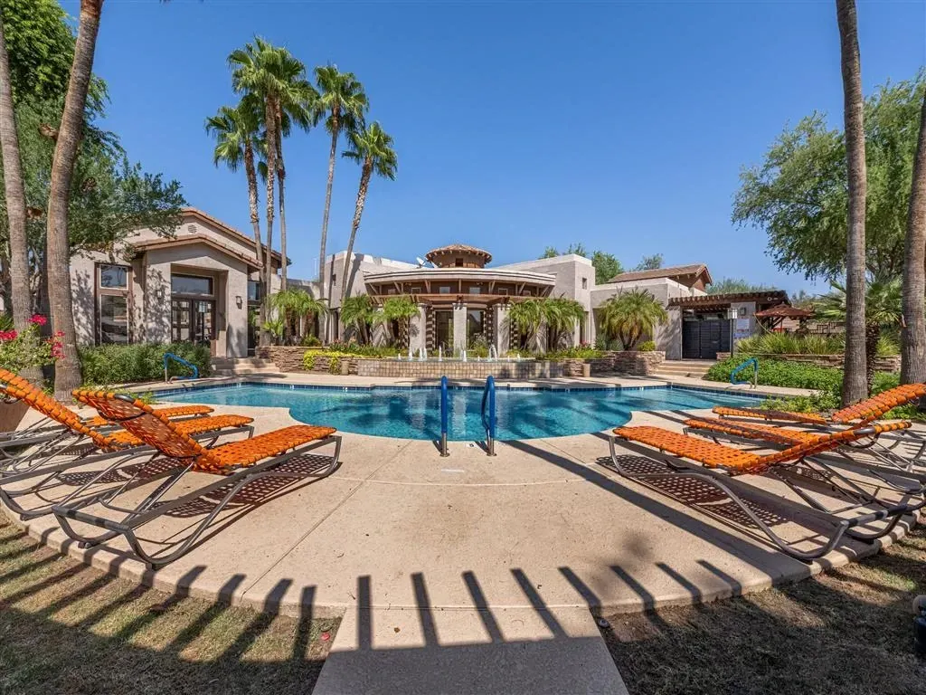 Outdoor swimming pool with lounge chairs and palm trees.